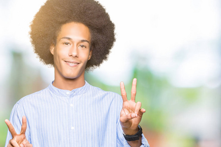 年轻的非裔美国人，有着非洲头发，微笑着看着镜头，手指在做胜利标志。 二号。