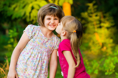 两个可爱的小妹妹在夏天公园的晴天笑着拥抱