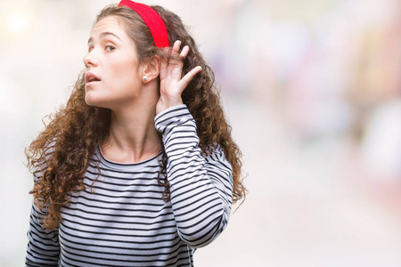 美丽的黑发卷发年轻女孩穿着条纹毛衣，在孤立的背景上微笑，用手捂住耳朵听谣言或流言蜚语。 耳聋概念。
