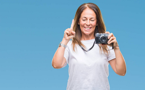 中年西班牙裔妇女用老式照片相机拍摄照片，背景偏僻，对一个想法或问题感到惊讶，用手指指着快乐的脸第一。