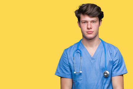 年轻的医生穿着医疗制服，在孤立的背景下放松，脸上有严重的表情。 简单自然地看着相机。