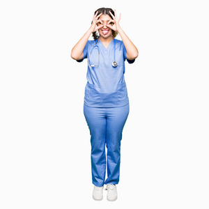 年轻的成年医生女士穿着医疗制服，做着好的手势，就像望远镜伸出舌头，透过手指看着眼睛。 疯狂的表情。
