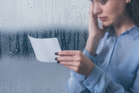 看到悲伤的女人拿着照片，用雨滴透过窗户哭泣