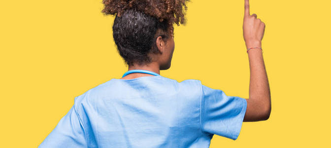 年轻的非裔美国医生女士，在孤立的背景下摆姿势，向后指向后面的手指手