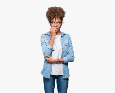 美丽的年轻的非洲裔美国妇女戴着眼镜，在孤立的背景上看起来压力和紧张，双手咬着嘴的指甲。 焦虑问题。