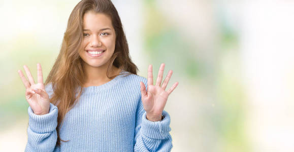 年轻漂亮的黑发女人穿着蓝色的冬季毛衣，在孤立的背景下，用手指举着8号，微笑着自信和快乐。