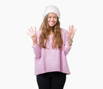 年轻漂亮的黑发女人，穿着毛衣和冬帽，在孤立的背景上，用手指数字9，微笑着自信和快乐。