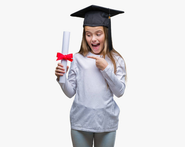 年轻漂亮的女孩戴着研究生帽，在孤立的背景下持有学位，非常高兴地用手和手指指指点点。