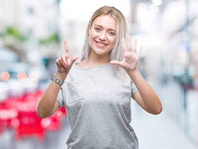 年轻的金发女子在孤立的背景显示和指向7号手指，同时微笑自信和快乐。