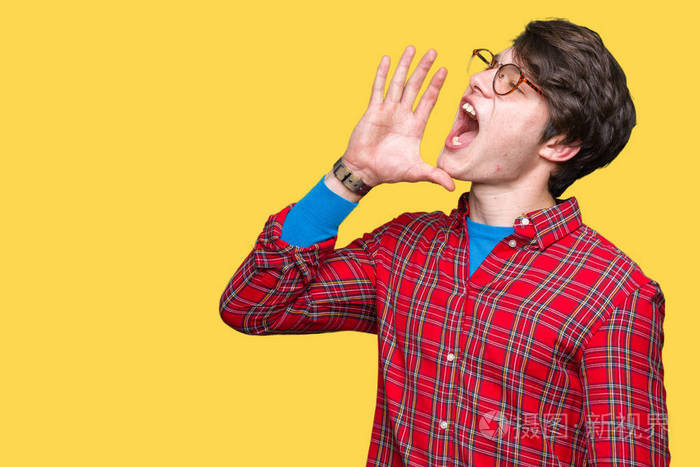 年轻的英俊男子戴着眼镜在孤立的背景上大声喊叫和尖叫,手在嘴上.