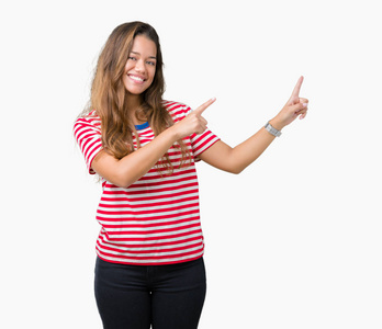 年轻漂亮的黑发女人穿着条纹T恤，在孤立的背景上微笑，看着相机，两只手和手指指向一边。