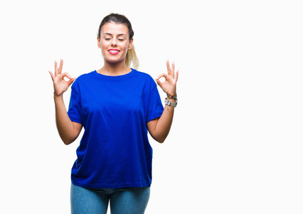 年轻漂亮的女人穿着休闲的蓝色T恤，在孤立的背景上放松，微笑着，闭上眼睛，用手指做冥想的手势。 瑜伽概念。