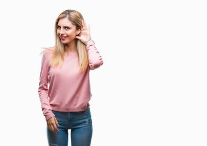 年轻漂亮的金发女人穿着粉红色的冬季毛衣，在孤立的背景上微笑，用手捂住耳朵听谣言或流言蜚语。 耳聋概念。