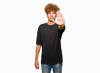 一个年轻英俊的男人，留着非洲头发，穿着黑色T恤，用手掌做着停止歌唱的动作。脸上带着消极严肃的手势的警告表情。
