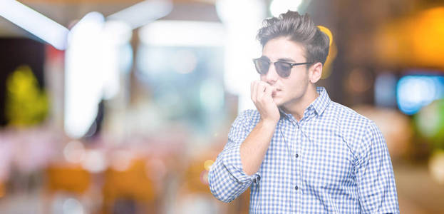 年轻的英俊男子戴着太阳镜，在孤立的背景上看着压力和紧张，双手咬着嘴的指甲。 焦虑问题。