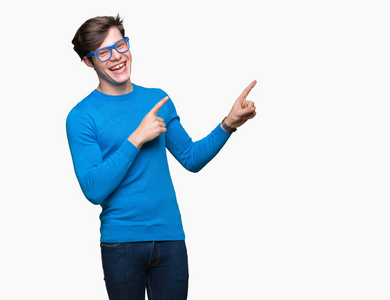 年轻的英俊男子戴着蓝色眼镜，在孤立的背景上微笑，看着相机，用两只手和手指指向一边。