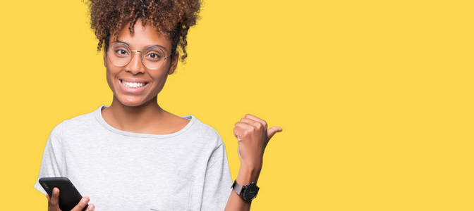 年轻的非裔美国妇女使用智能手机，在孤立的背景上指指点点，并用拇指向侧面展示，脸上洋溢着幸福的笑容