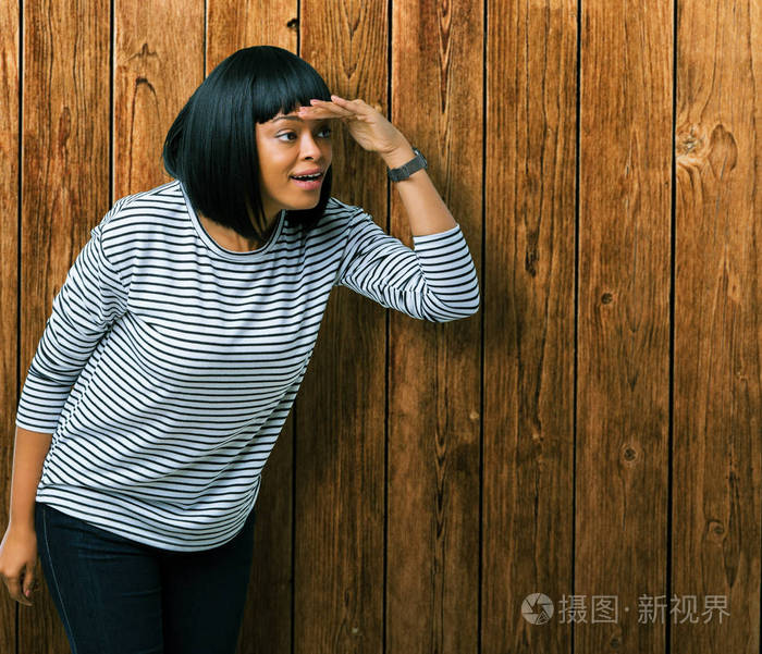 穿着条纹毛衣,在孤立的背景上,非常高兴和微笑,用手捂住头看着远方