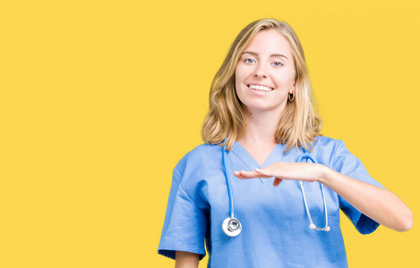 美丽的年轻医生女士穿着医疗制服，在孤立的背景上做手势，双手显示大尺寸的标志符号。 微笑着看着相机。 测量概念。