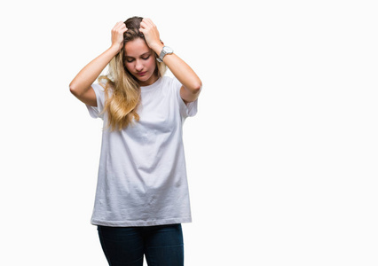 年轻漂亮的金发女人穿着休闲的白色T恤，在孤立的背景下，因为头痛绝望和压力，因为疼痛和偏头痛。 手放在头上。