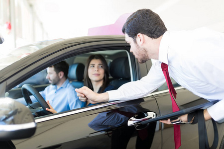 严肃的经销商看着一对夫妇坐在车里调查经销商的汽车特征