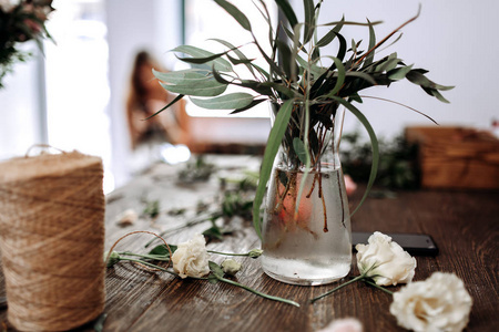 花店的桌子上有一个花瓶, 里面有水和树枝, 还有绿叶和绳子的