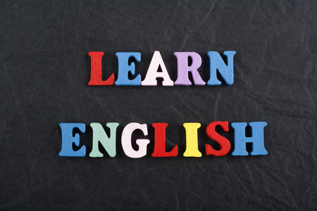 黑色黑板背景上的LEARN英语单词由彩色ABC字母组成，木质字母，广告文本的复制空间。学习英语