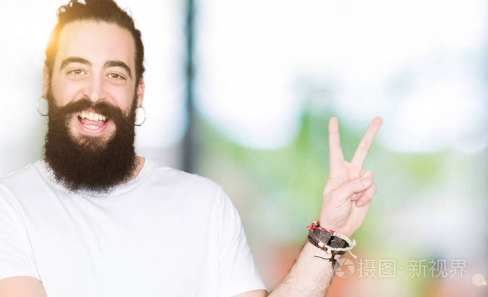 年轻的时髦男人,留着长发和胡须,穿着休闲的白色t恤,微笑着,开心地