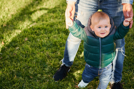 s hand and learning to walk in a park on sunny day. Father and s