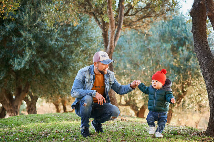 阳光明媚的一天,可爱的小男孩和他的父亲一起在公园里散步. 一对父子.