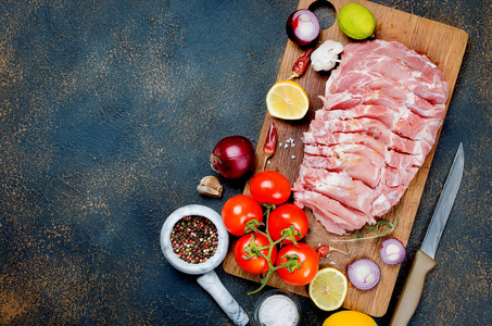 用蔬菜和香料在厨房板上烘烤的大块生猪肉，深色背景，俯视空间