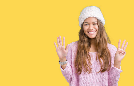 年轻漂亮的黑发女人，穿着毛衣和冬帽，在孤立的背景上，用手指举着8号，微笑着自信和快乐。