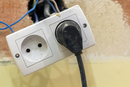 双插座电源插座，连接电动隔离彩色电线，塑料插头安装在浅黄色抹灰墙上。 家庭内部电工工作理念。
