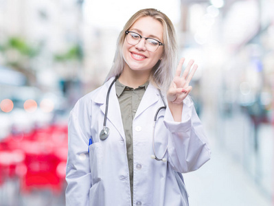年轻的金发医生女人在孤立的背景显示和指着第三个手指，同时微笑自信和快乐。