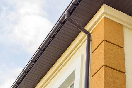 关闭别墅角落的细节与棕色金属木板壁板和屋顶与钢沟雨系统。 屋面施工排水管安装与连接理念。