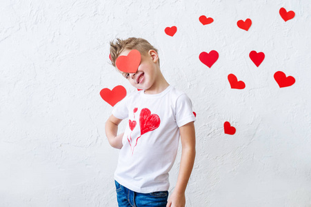 有趣的肖像，微笑的男孩隐藏他的眼睛与红色的心脏形状摆在工作室。 情人节的概念。