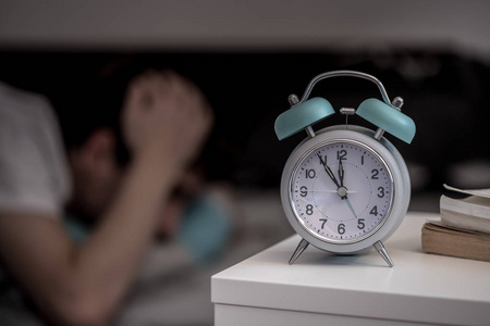 床头柜上有白色闹钟。 年轻人试图在失眠的背景下睡觉