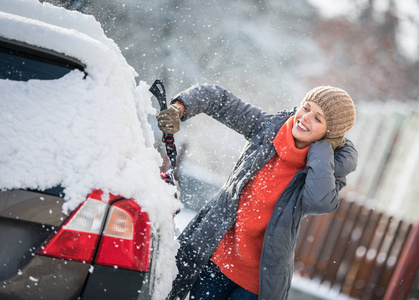 大雪后，一位漂亮的年轻女士在雪地上清洁她的汽车彩色色调图像