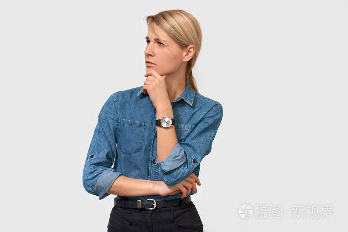 照片 不信任的沉思的年轻商务女性穿着牛仔衬衫,手指触摸她的下巴