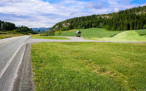 挪威山区的沥青路。 农业领域。 公共汽车站。 对于木材可见的村庄。
