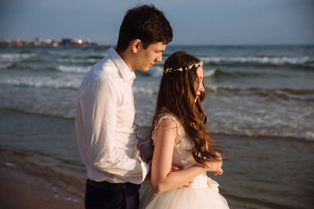 新郎在沙滩上的日落美景中拥抱美丽的新娘。新婚夫妇在婚礼上呆在一起
