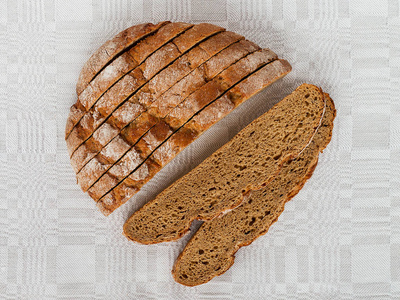 切片圆形黑麦面包，在灰色亚麻桌布上有一个令人开胃的脆皮棕色面包皮。美味，有用，营养丰富。正上方查看，特写..