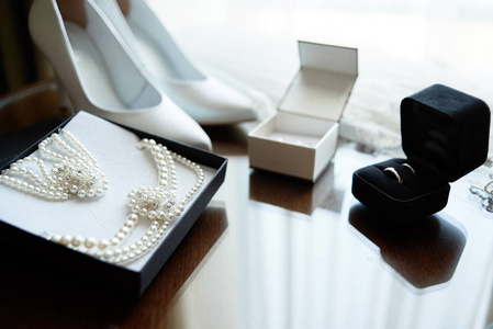 豪华新娘首饰珍珠项链和手镯和白色女鞋，金色结婚戒指模糊在木制背景，复制空间。结婚的早晨。新娘饰品。婚姻概念