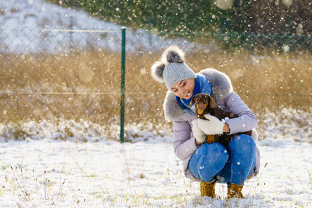 年轻的女人在冬天玩得很开心。 白雪皑皑的白雪中，一只母狗在玩她的小纯种狗狗