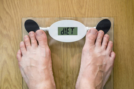 男子站在体重秤饮食推荐文本的规模。 饮食词汇体重秤屏幕与男子脚