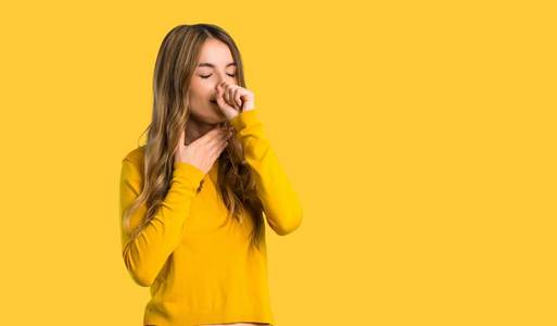 带黄色毛衣的年轻女孩咳嗽,而且在与世隔绝的黄色背景下感到很难受