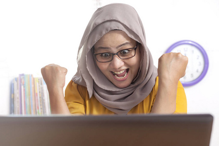 亚洲穆斯林女士的肖像在收到她的电子邮件中的好消息后，表现出快乐惊讶的表情，庆祝胜利的姿态