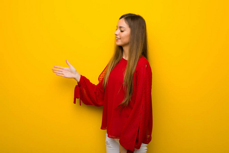 年轻女孩穿着红色的衣服在黄色的墙上握手后好