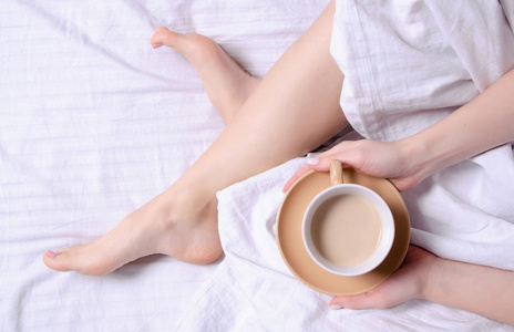 妇女拿着一杯咖啡在白色亚麻布床