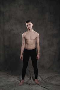 一名年轻的男性芭蕾演员, 穿着黑色的长裤和的躯干, 在灰色的粗野背景下表演舞蹈动作, 灯光和浓烟